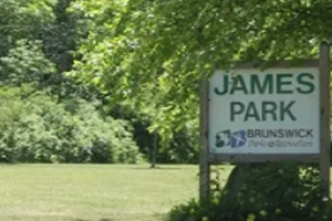 Sign for "James Park" in front of a grassy area and trees.